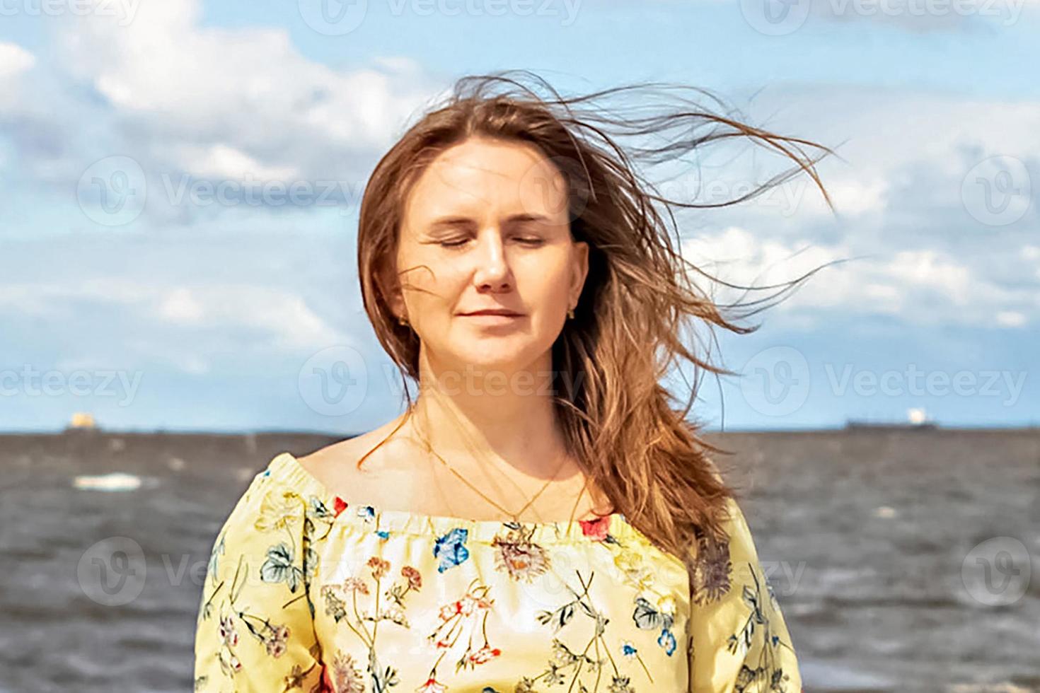 un' grande ritratto di un' giovane donna con svolazzanti capelli nel il vento su il riva del mare foto