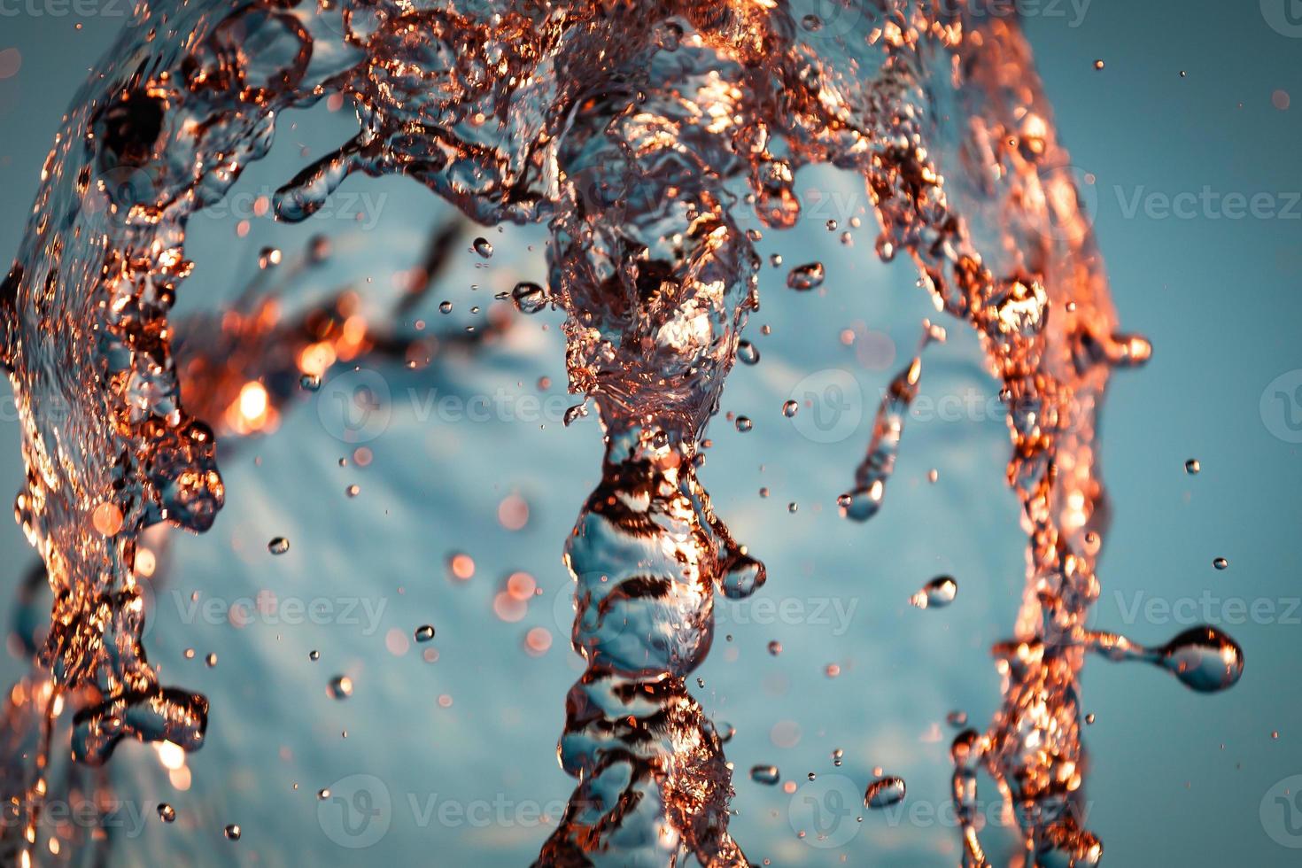 getti di acqua con un' lotto di gocce e bolle sotto il raggi di il sole su un' blu sfondo. un' grande Piano il struttura di il acqua onde di un' grande Fontana foto