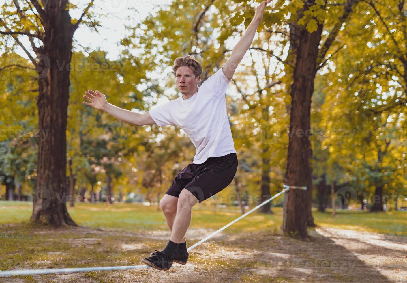 giovane uomo equilibratura e salto su slackline. uomo a passeggio, salto e equilibratura su corda nel parco. foto