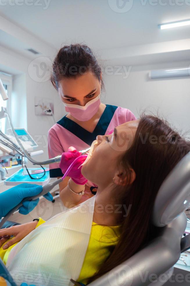 dentista nel rosa uniforme trattare il denti di un' paziente foto