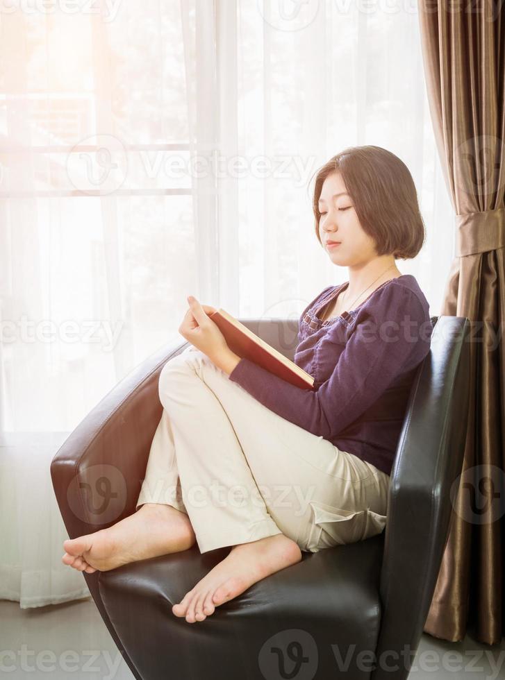 giovane asiatico donna corto capelli leggere un' libro nel vivente camera foto