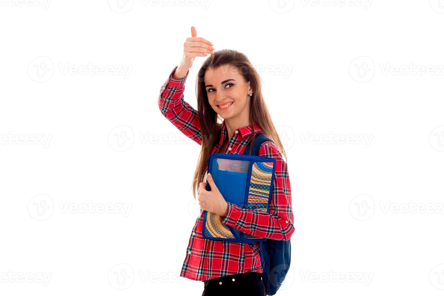 contento elegante inteligente alunno ragazza con zaino su sua le spalle e cartelle per i Quaderni nel mani mostrando pollici su e sorridente su telecamera isolato su bianca sfondo foto