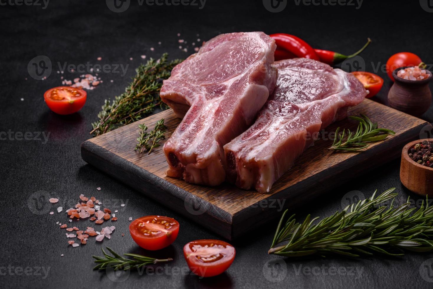 fresco crudo Maiale carne su il costolette con spezie e erbe aromatiche su un' di legno taglio tavola foto