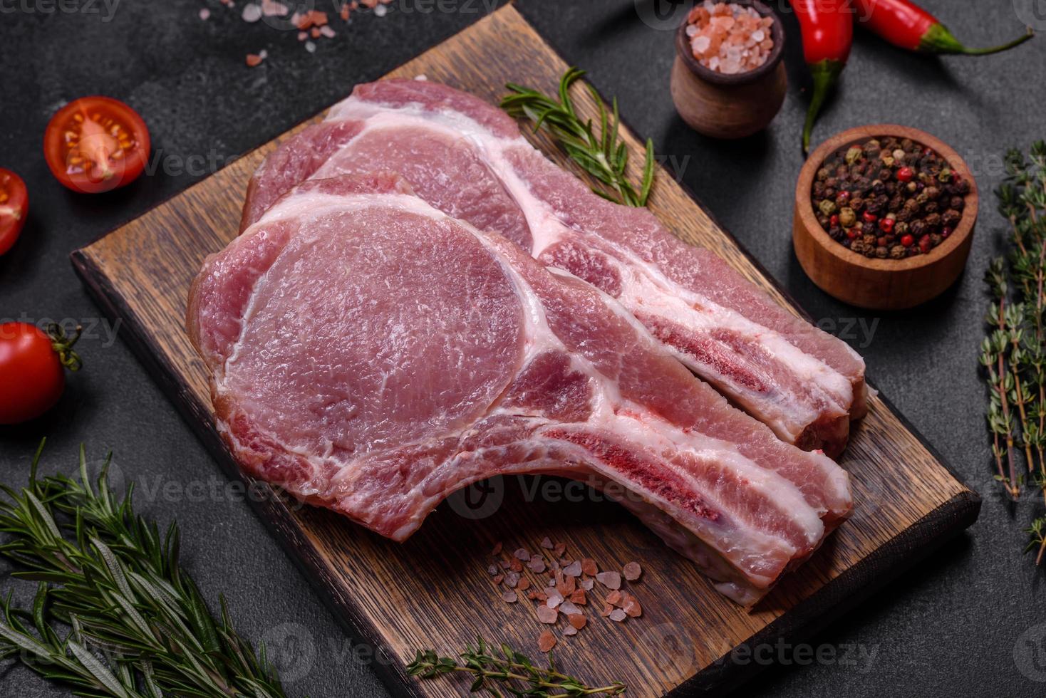 fresco crudo Maiale carne su il costolette con spezie e erbe aromatiche su un' di legno taglio tavola foto