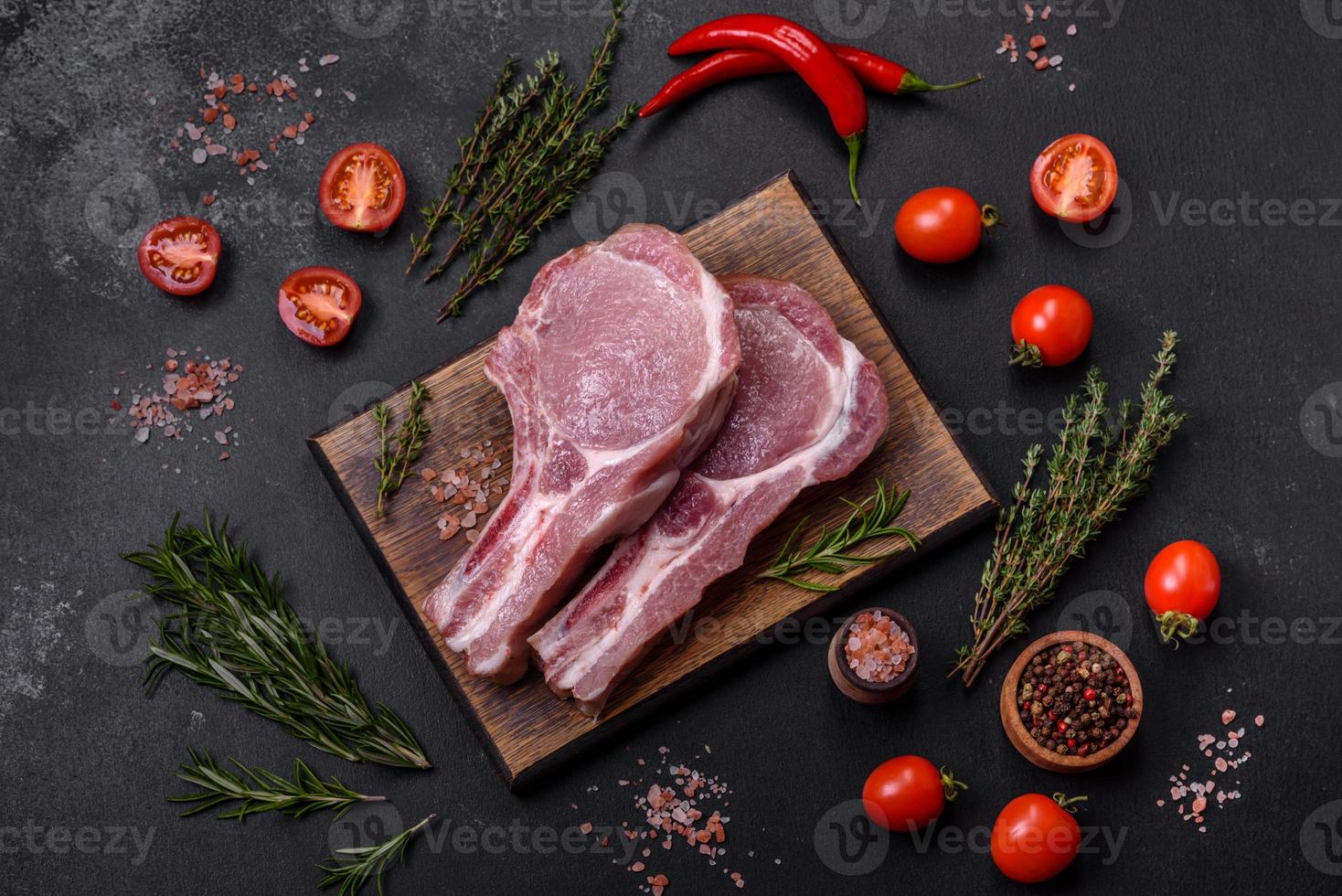 fresco crudo Maiale carne su il costolette con spezie e erbe aromatiche su un' di legno taglio tavola foto