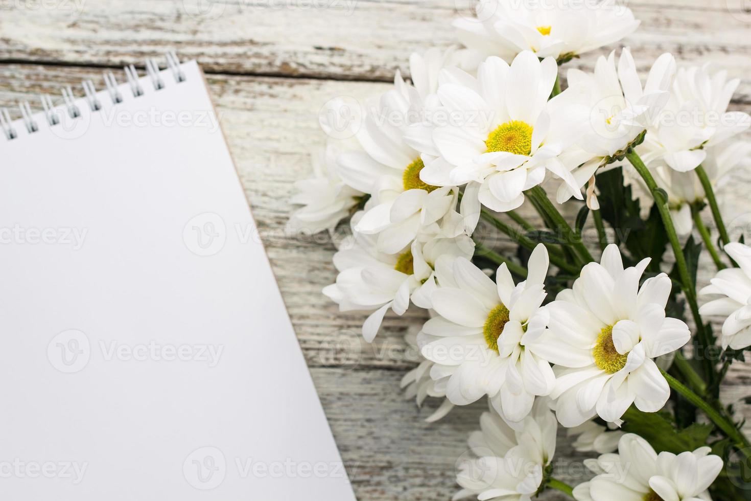 primavera mazzo di bianca margherite con pulito taccuino per Scrivi su bianca di legno tavolo foto