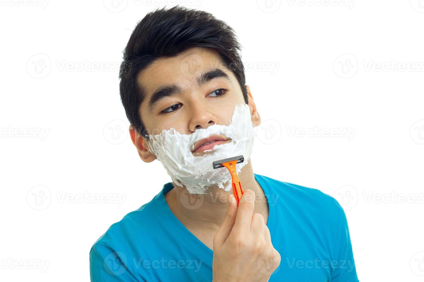 bello giovane tipo con nero capelli e un' schiumogeno facciale si rade il suo barba avvicinamento foto