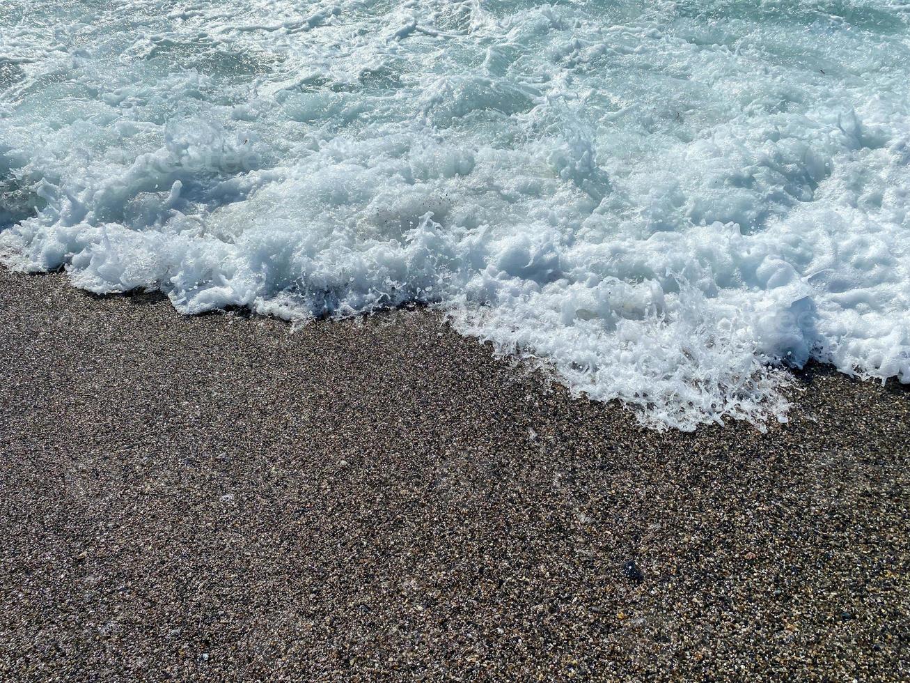 onde di acqua nel il mare e sabbia con piccolo naturale multicolore pietre su il riva del mare, piccolo ciottoli su il spiaggia. sfondo, struttura foto