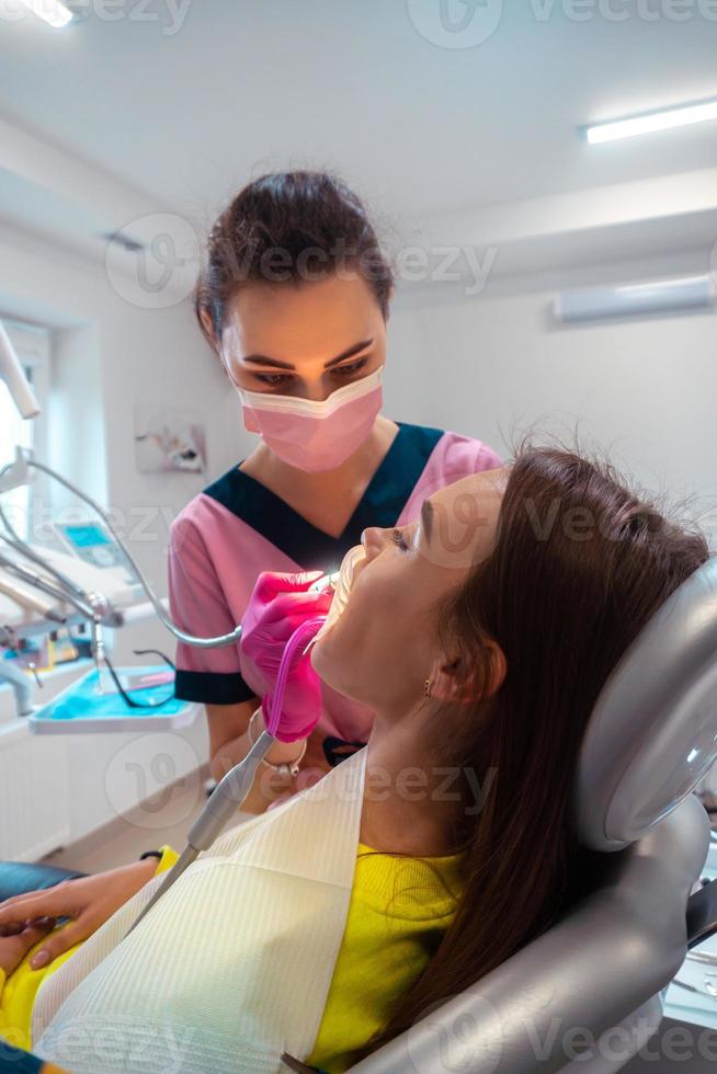 dentista nel rosa uniforme trattare il denti di un' paziente foto