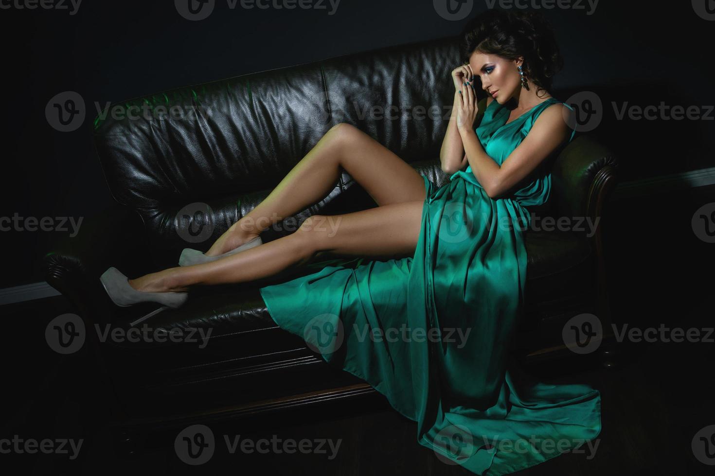 donna indossare bellissimo verde seta vestito è in posa su pelle divano foto