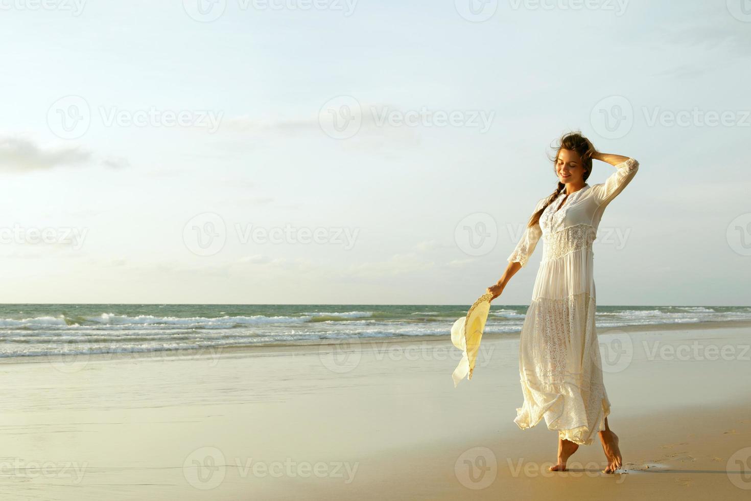 donna indossare bellissimo bianca vestito è a piedi su il spiaggia durante tramonto foto