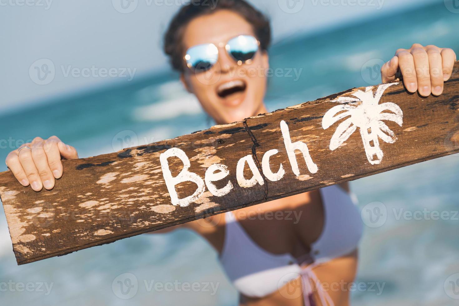 contento indossare costume da bagno con vecchio di legno cartello su il spiaggia foto