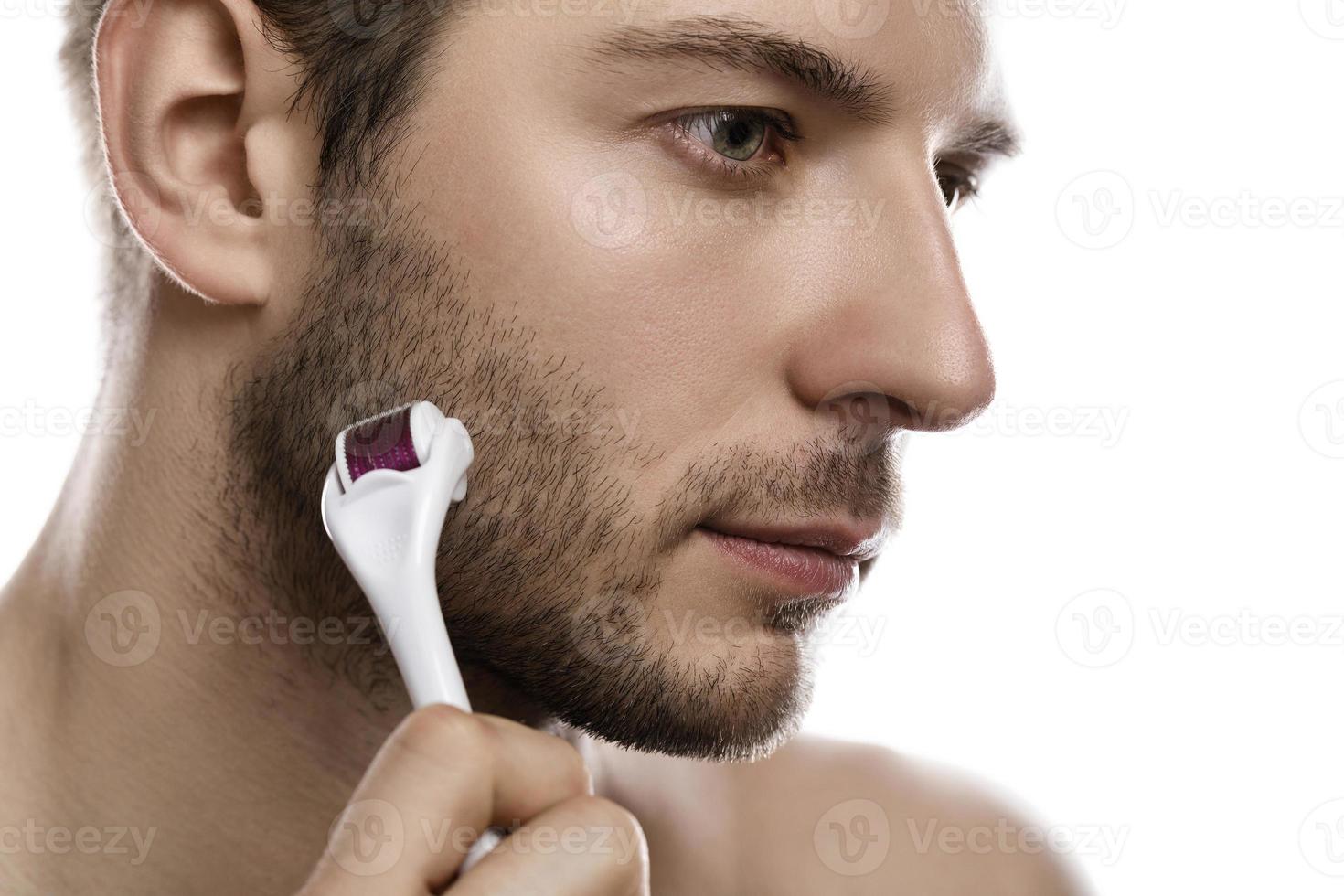 giovane bello uomo è utilizzando derma rullo per barba crescita foto