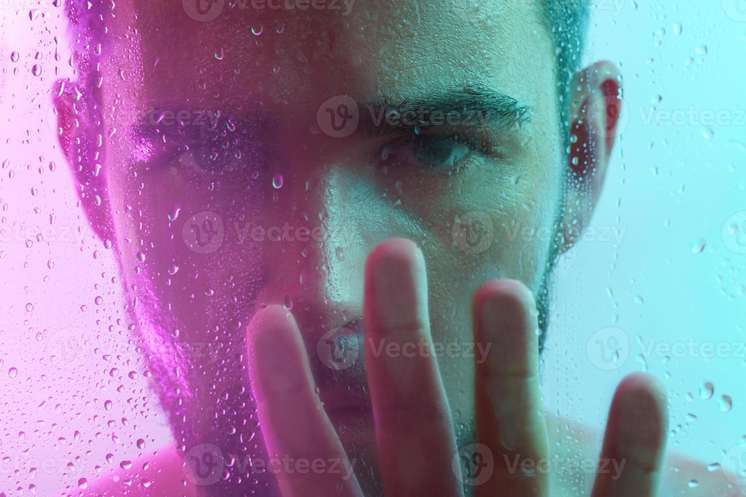 ritratto di bello uomo attraverso bagnato bicchiere nel neon leggero foto