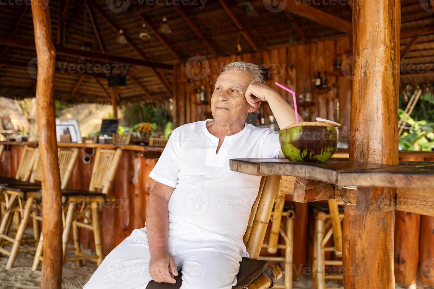 contento anziano uomo è potabile un' Noce di cocco acqua nel il spiaggia bar foto