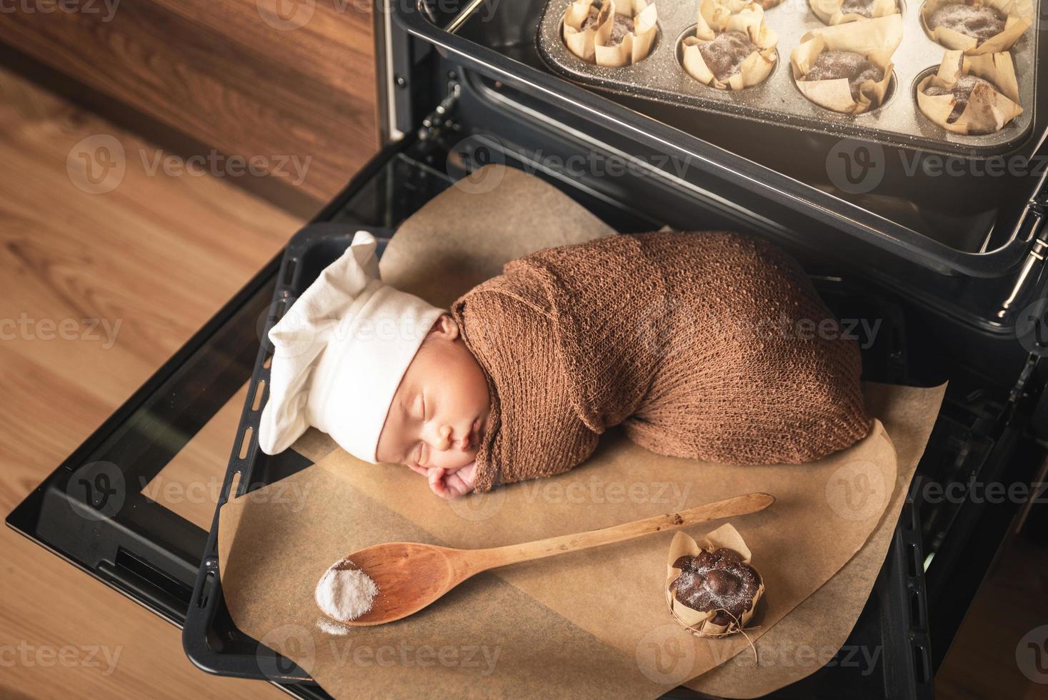 neonato bambino indossare dello chef cappello è dire bugie su il forno vassoio con un' muffin foto