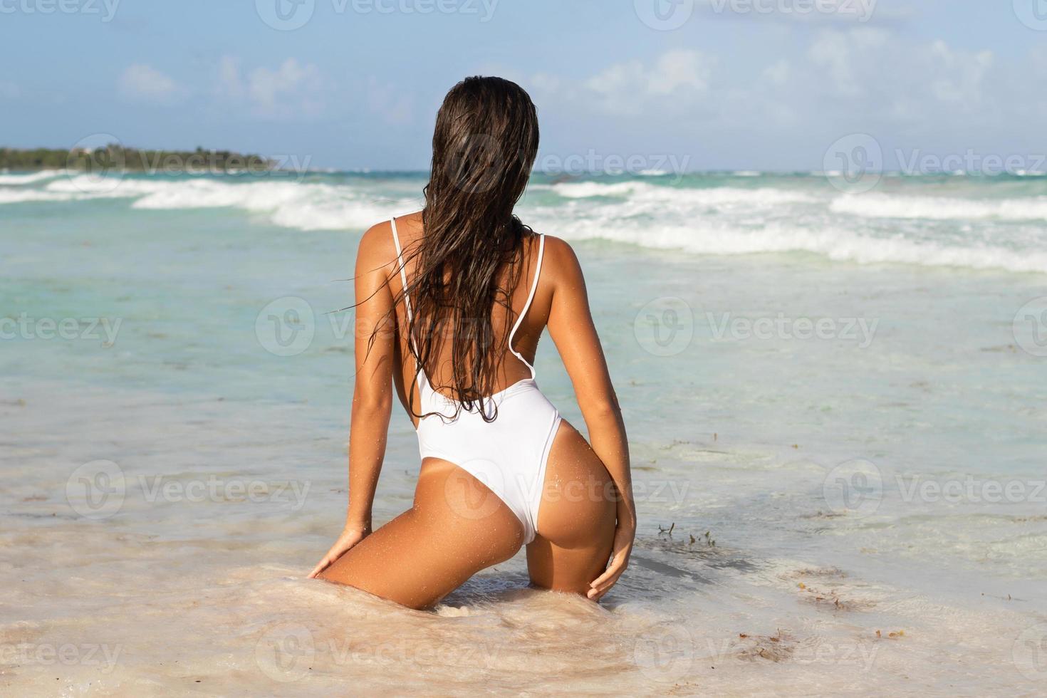sexy donna indossare bianca costume da bagno è in posa su il spiaggia foto