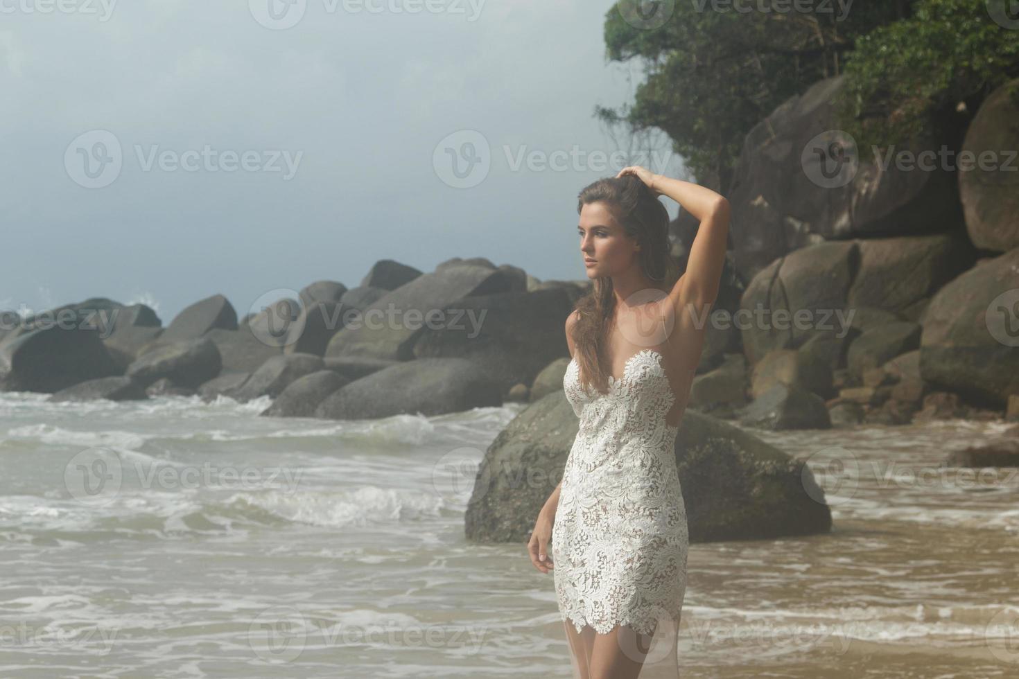 giovane donna indossare bellissimo bianca vestito è in posa su il spiaggia foto