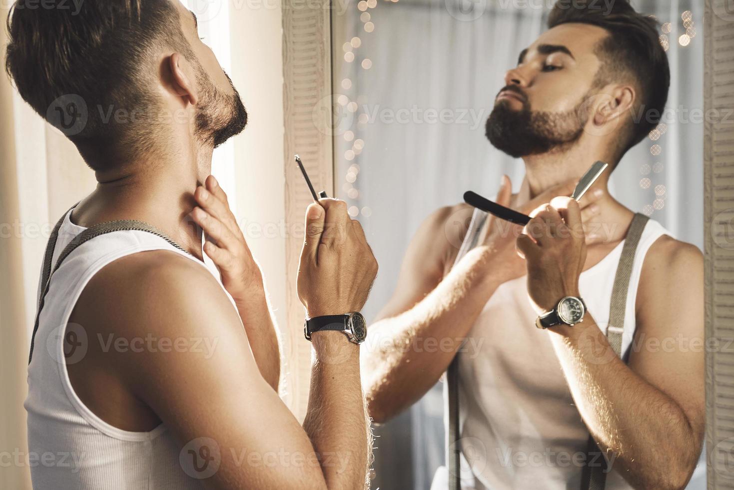uomo guardare nel il specchio e rasatura il suo barba con un' dritto rasoio foto