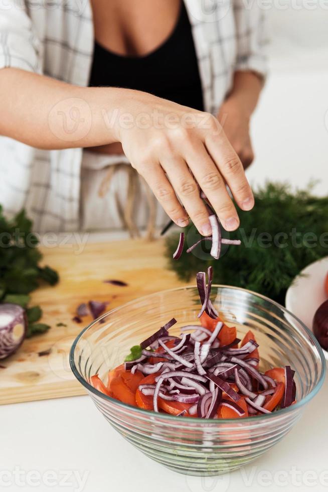 femmina mani cucinando vegetariano insalata e aggiungendo rosso cipolla per esso foto