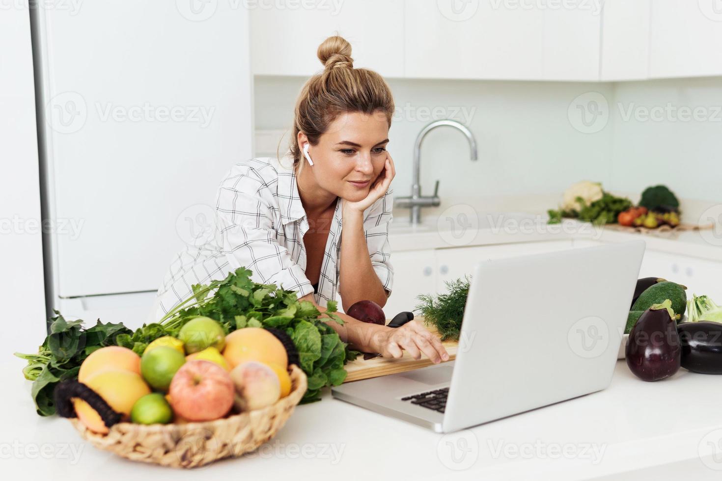 giovane bella donna utilizzando il computer portatile per in linea ricetta ricerca per cucinare a casa foto