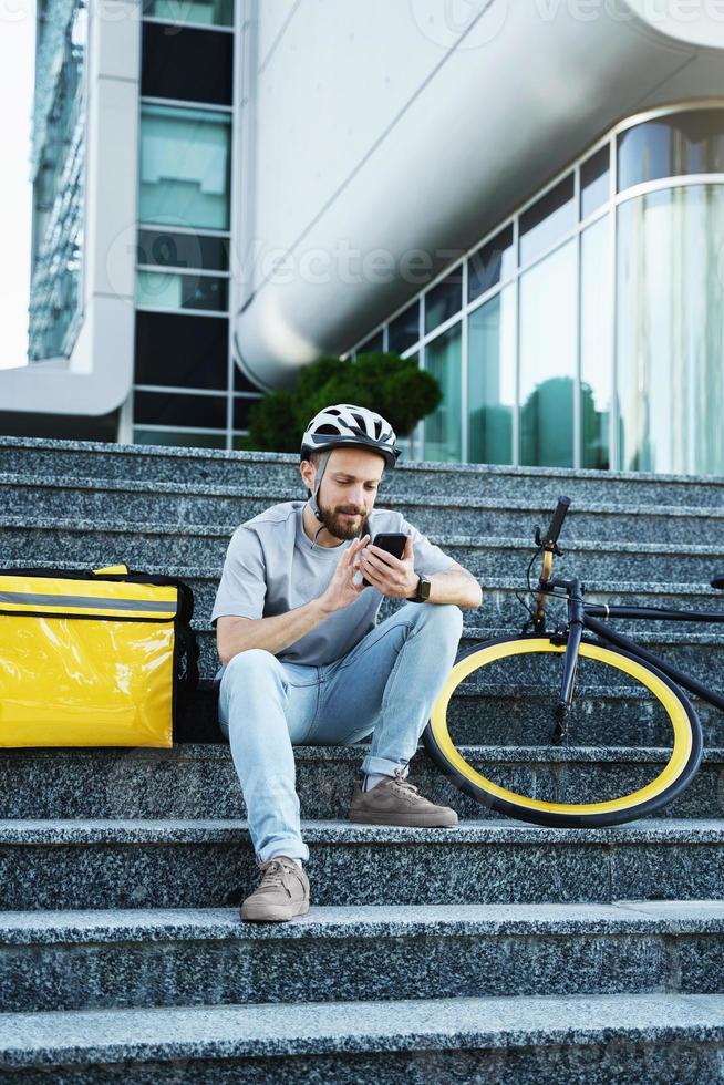 esprimere cibo consegna Corriere seduta su il le scale con isolato Borsa e bicicletta. foto