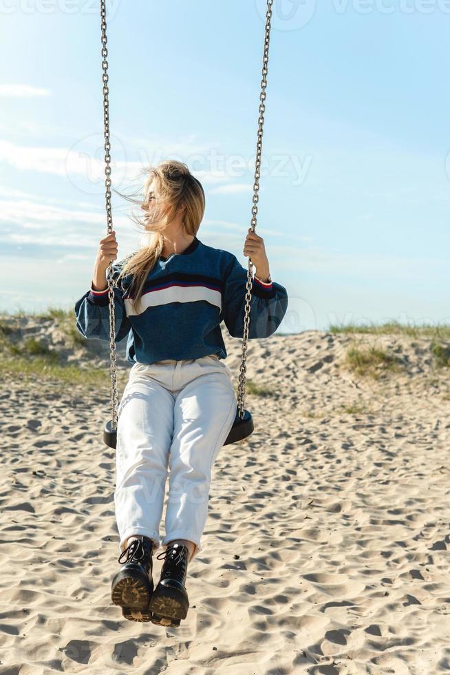 giovane donna oscillante su il swing e guardare lontano a il sabbioso spiaggia. foto