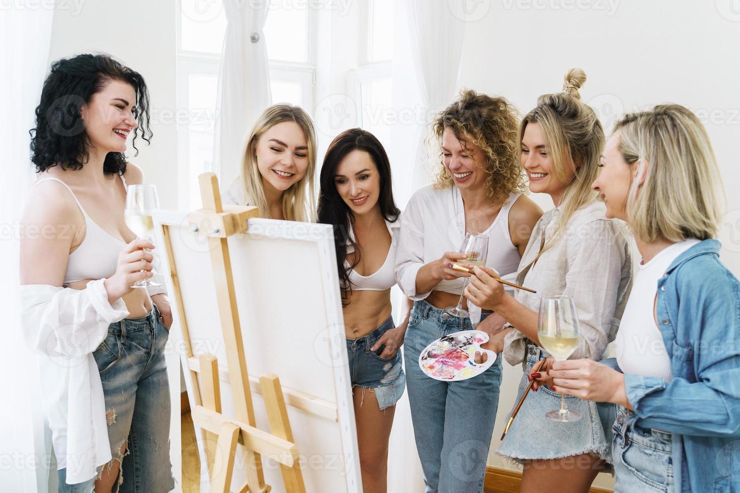 gruppo di donne dipingere su tela e potabile bianca vino durante festa a casa foto