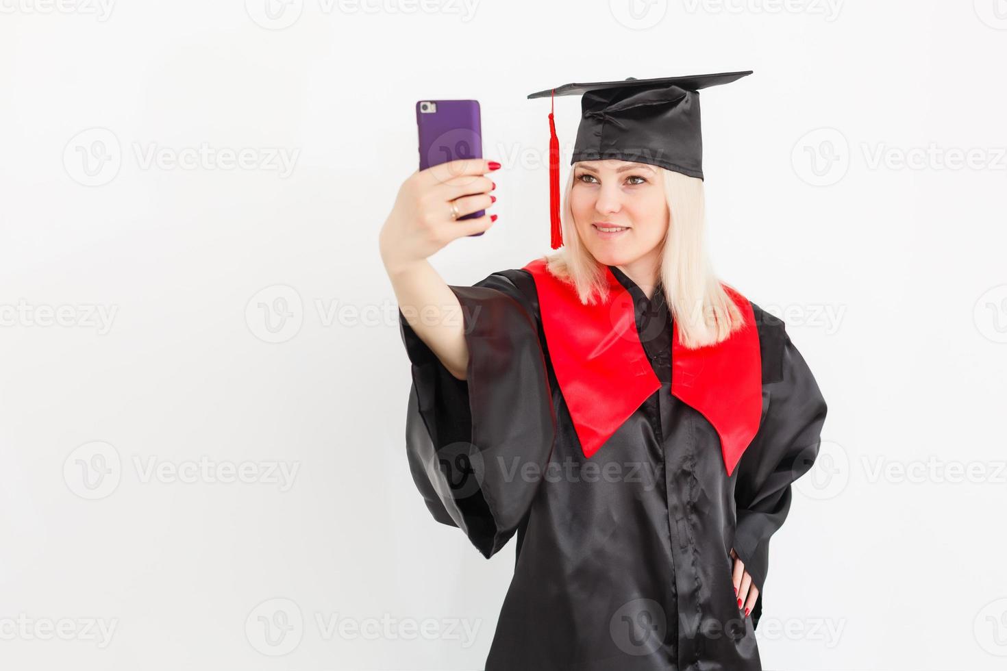 eccitato contento femmina alunno diplomato è in piedi nel Università sala nel mantello con diploma nel mano, sorridente e guardare a il telecamera foto