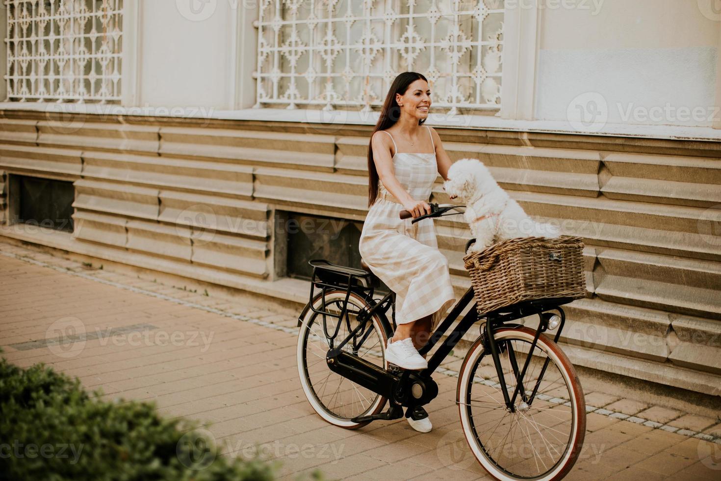 giovane donna con cane bianco bichon frise nel cestino della bici elettrica foto