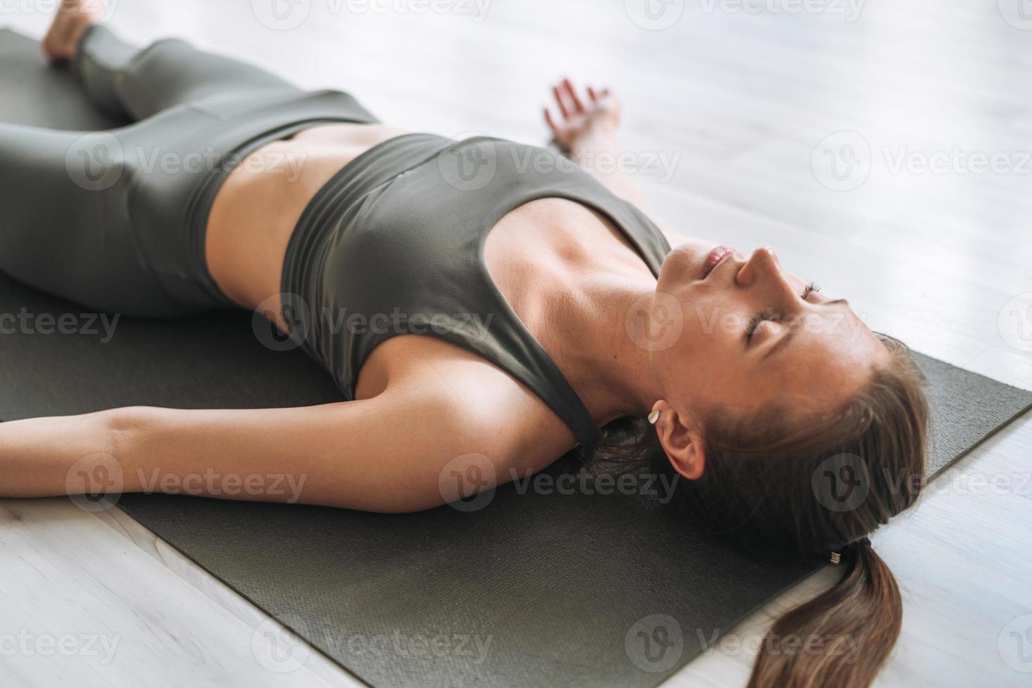 giovane in forma donna pratica yoga fare savasana nel leggero yoga studio con verde Casa pianta foto