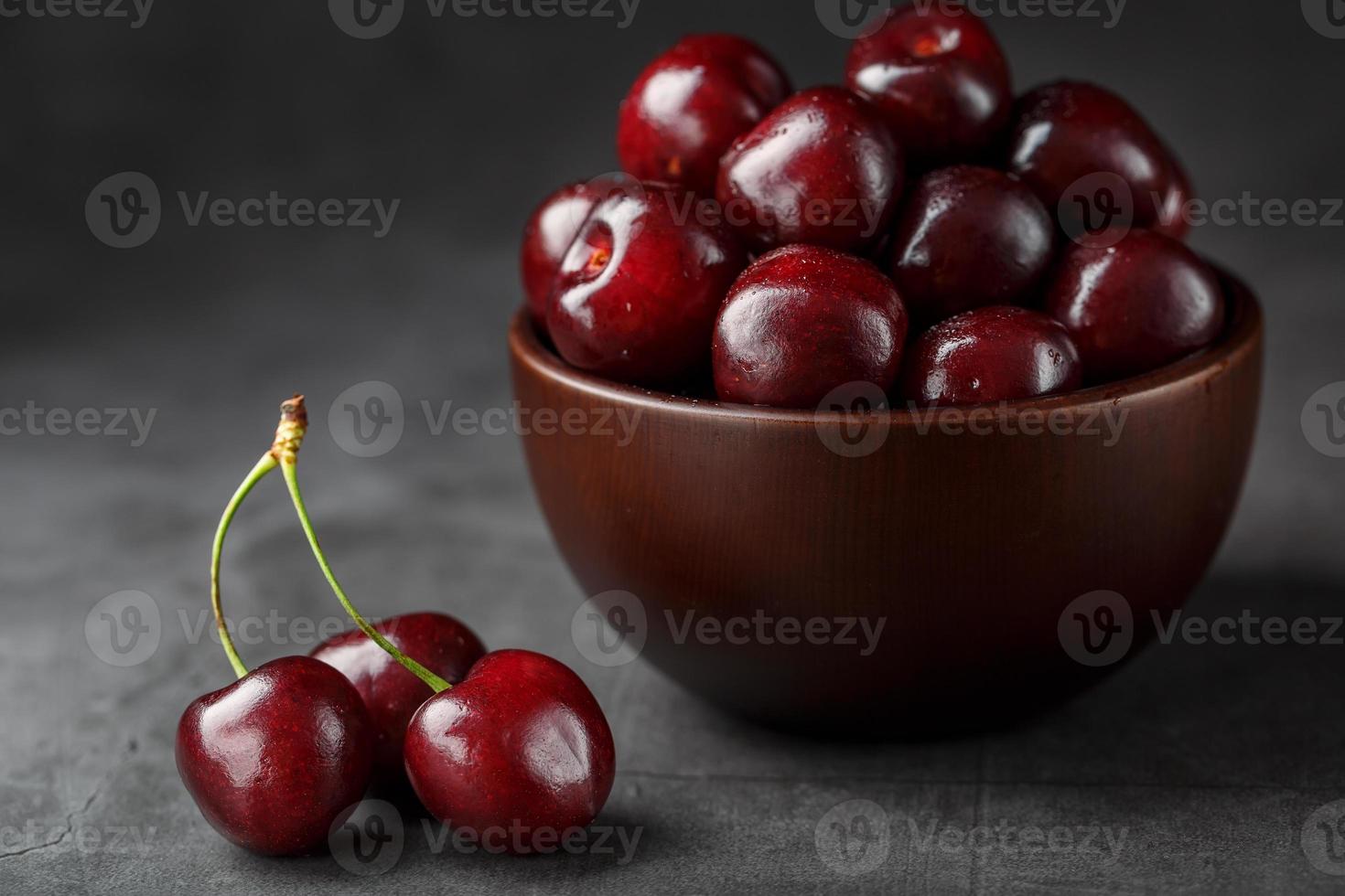 maturo e succoso ciliegia frutti di bosco su un' nero strutturale sfondo nel un' Marrone tazza, con acqua gocce. superiore Visualizza, avvicinamento. foto