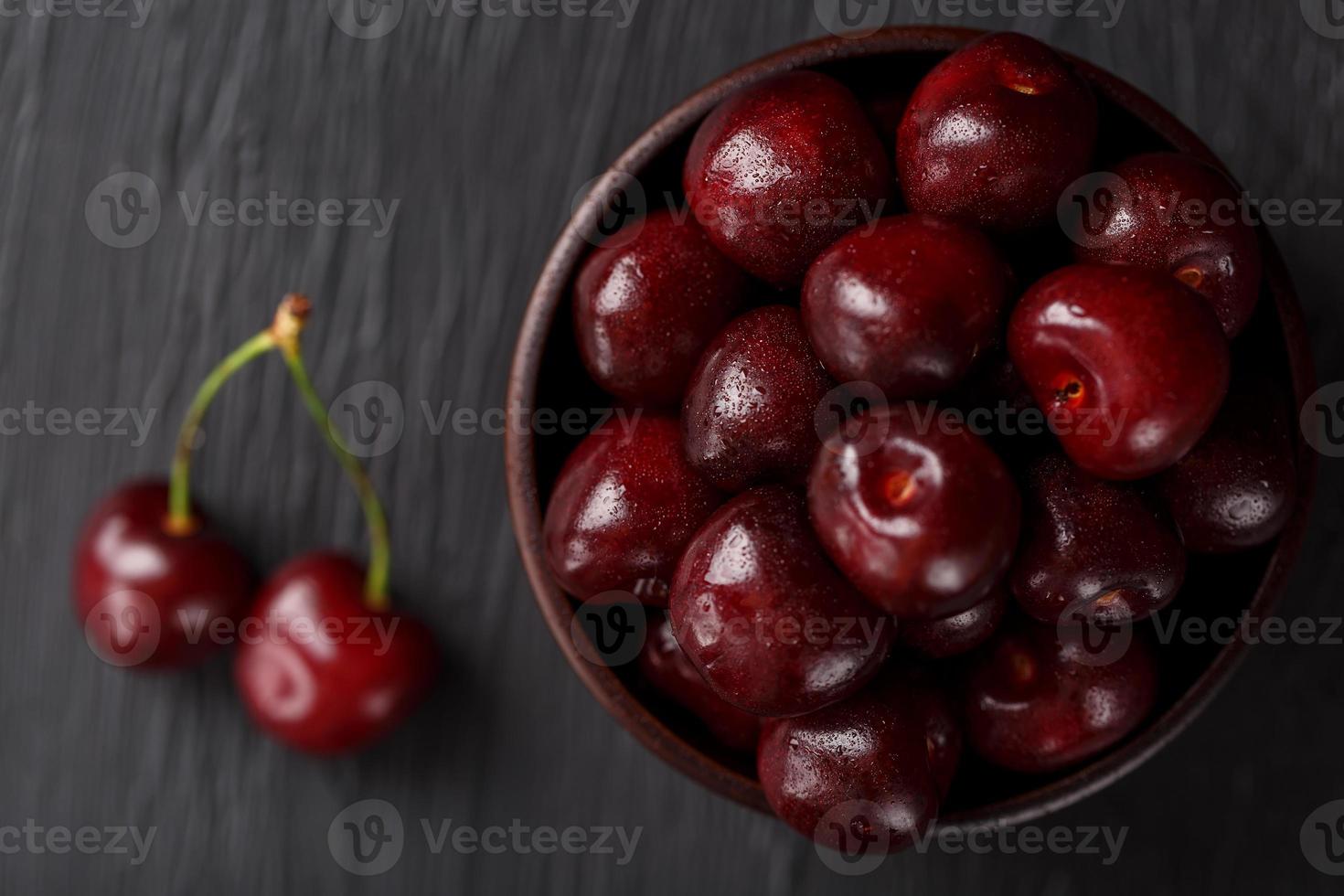 maturo e succoso ciliegia frutti di bosco su un' nero strutturale sfondo nel un' Marrone tazza, con acqua gocce. superiore Visualizza, avvicinamento. foto