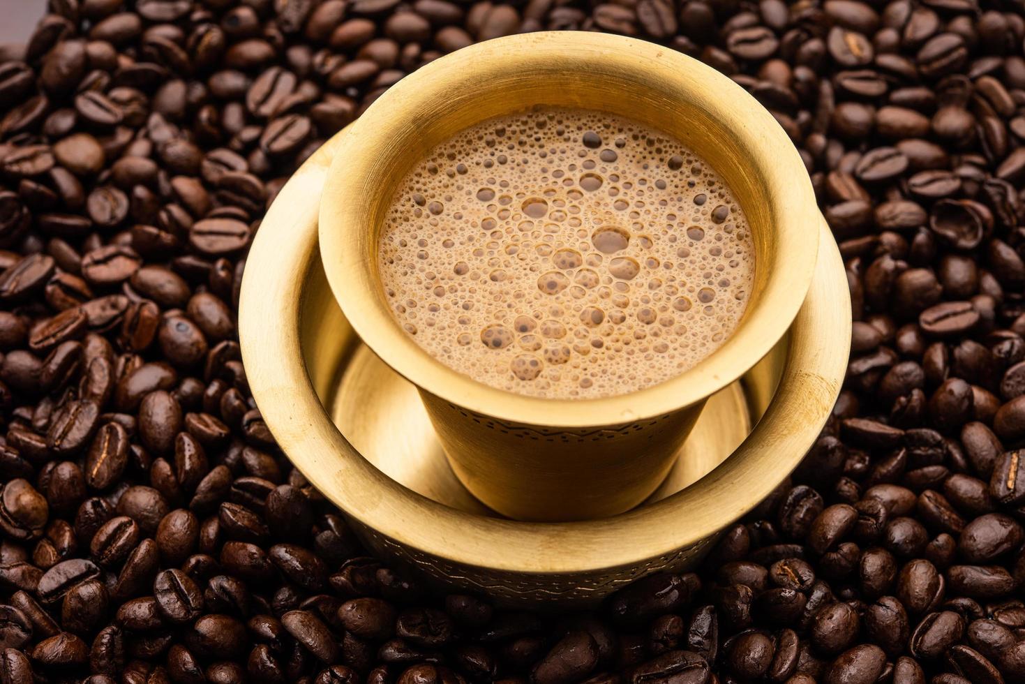 Sud indiano filtro caffè servito nel un' tradizionale bicchiere o tazza al di sopra di arrostito crudo fagioli foto