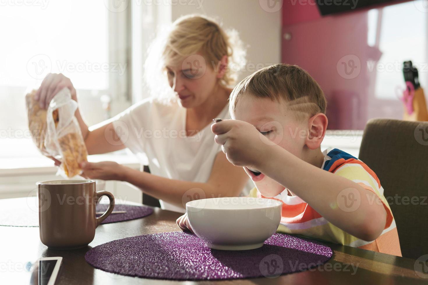 bellissimo madre e sua carino figlio mangiare salutare fiocchi di mais per prima colazione foto