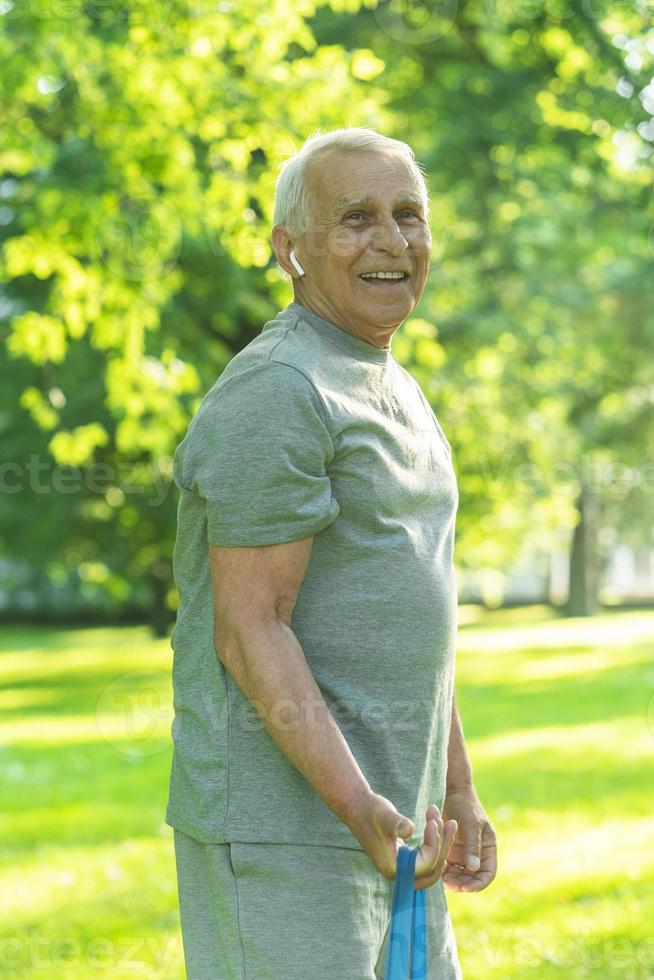 attivo anziano uomo esercizio con un' gomma da cancellare resistenza gruppo musicale nel verde città parco foto