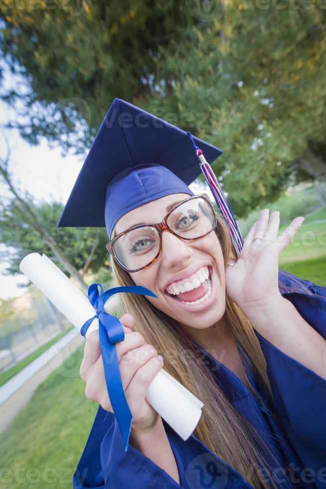 espressive giovane donna Tenere diploma nel berretto e toga foto