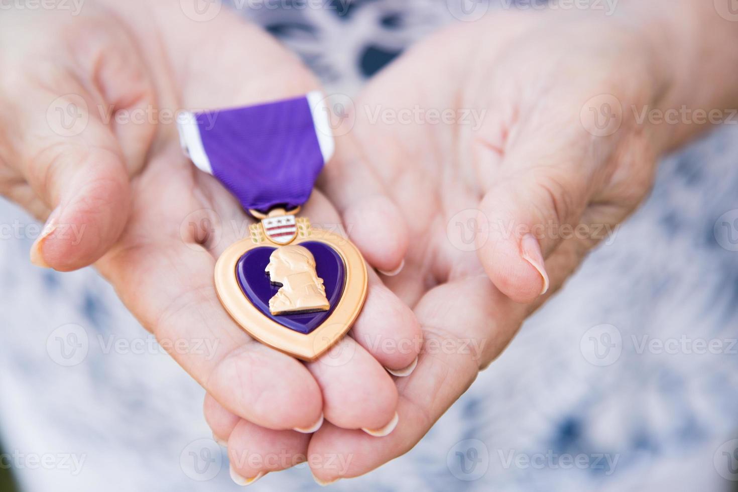 anziano donna Tenere il militare viola cuore medaglia nel sua mani. foto