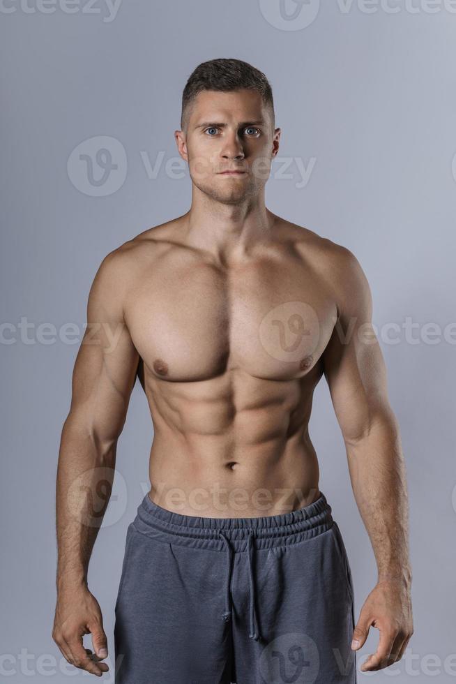 bodybuilder mostrando il suo muscolare corpo contro grigio sfondo foto