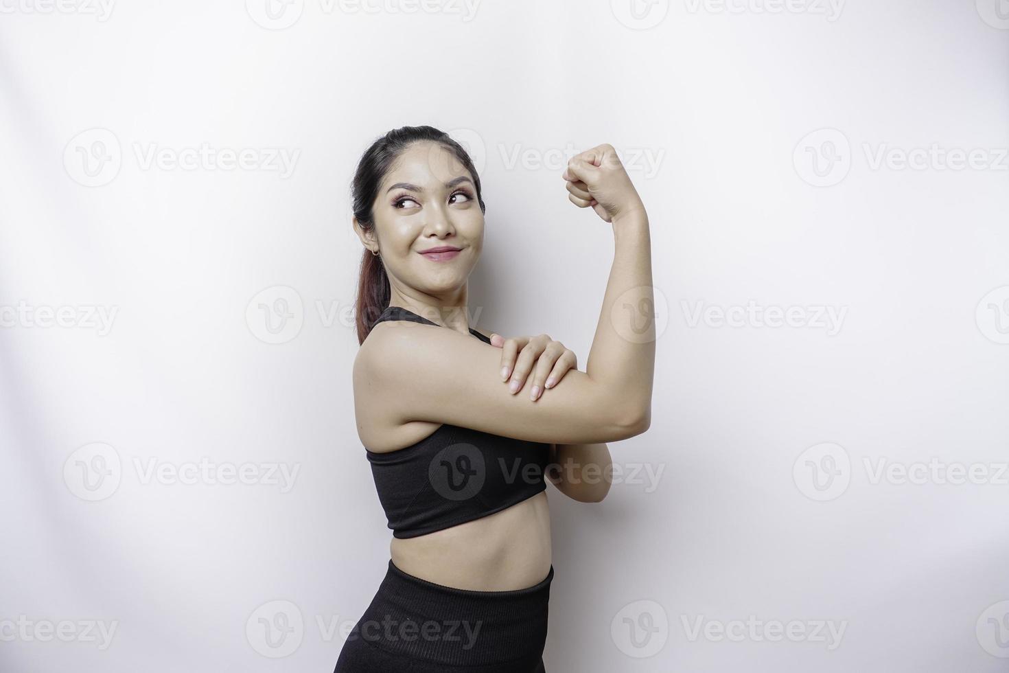 eccitato asiatico sportivo donna indossare un' abbigliamento sportivo mostrando forte gesto di sollevamento sua braccia e muscoli sorridente con orgoglio foto