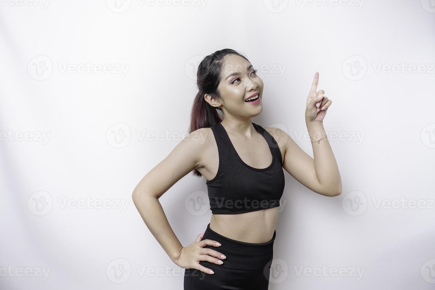 eccitato asiatico sportivo donna indossare abbigliamento sportivo puntamento a il copia spazio su superiore di suo, isolato di bianca sfondo foto
