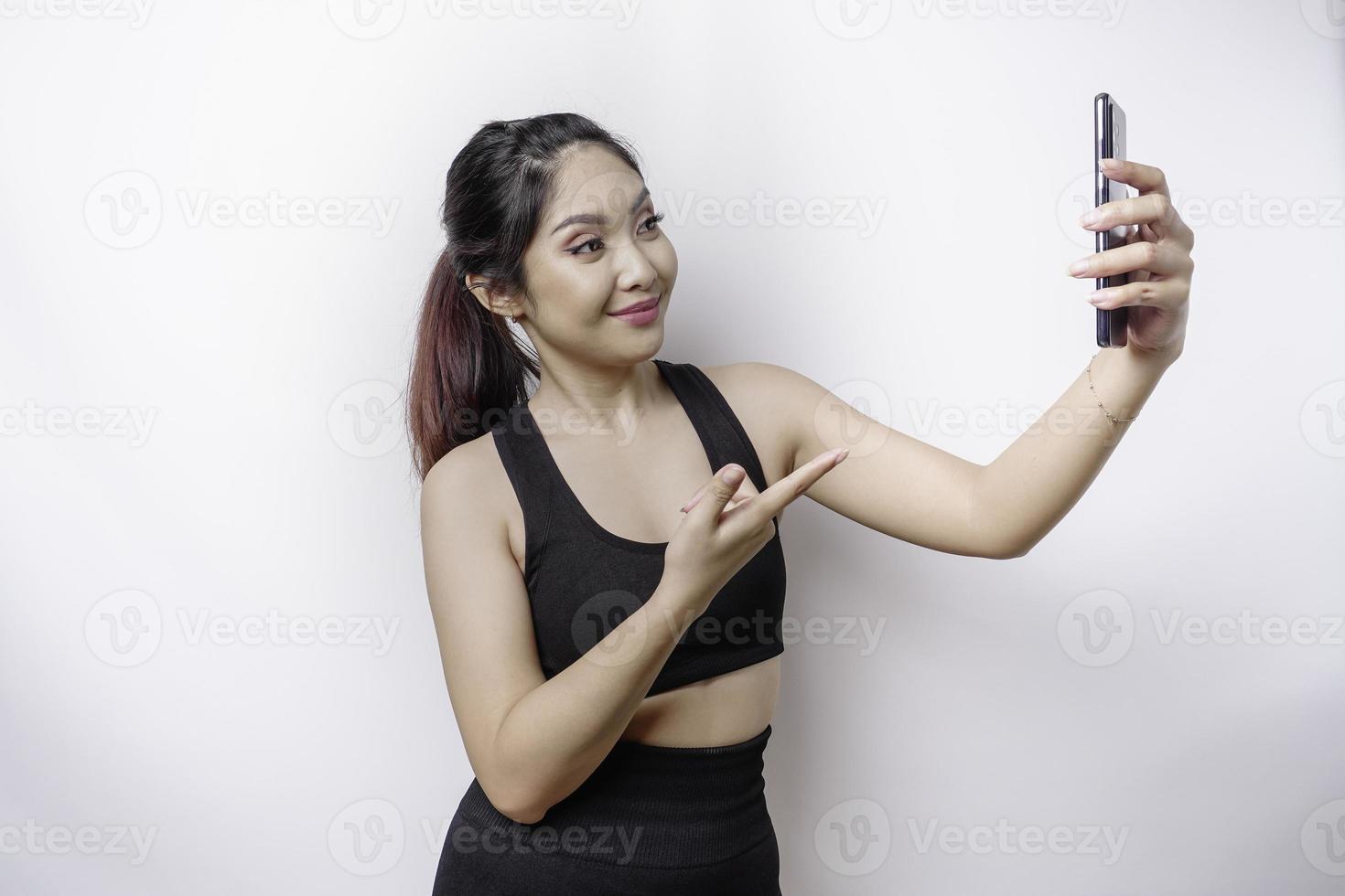 un' ritratto di un' sportivo asiatico donna indossare un' abbigliamento sportivo e Tenere sua Telefono, isolato di bianca sfondo foto