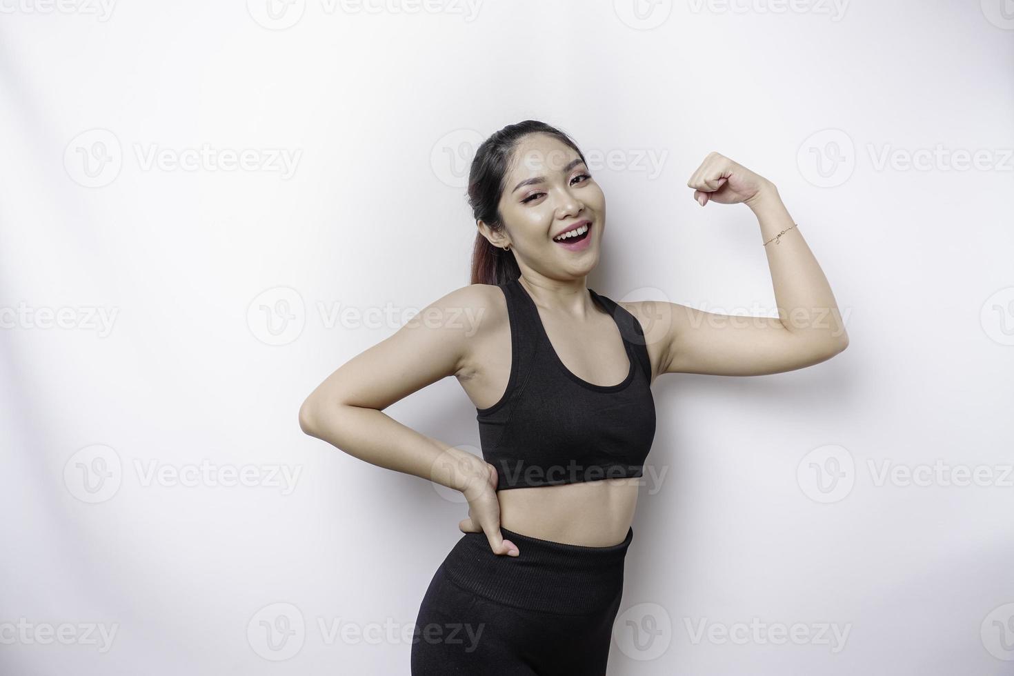 eccitato asiatico sportivo donna indossare un' abbigliamento sportivo mostrando forte gesto di sollevamento sua braccia e muscoli sorridente con orgoglio foto