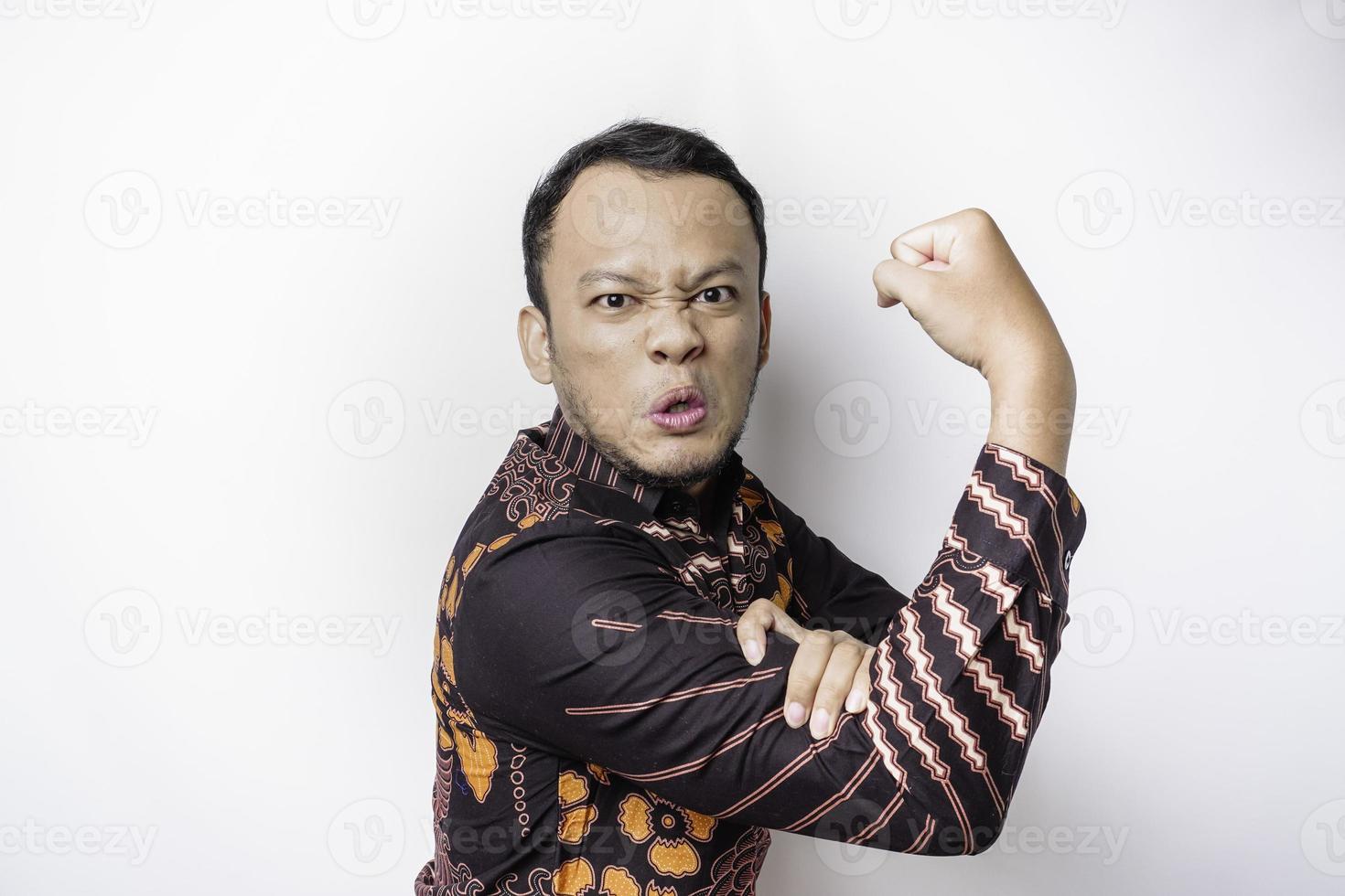 eccitato asiatico uomo indossare batik camicia mostrando forte gesto di sollevamento il suo braccia e muscoli sorridente con orgoglio foto