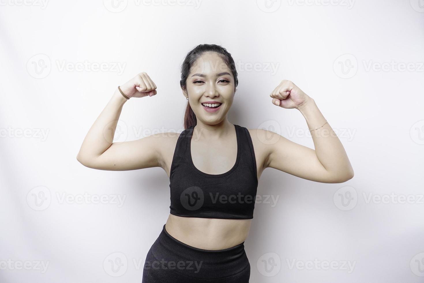 eccitato asiatico sportivo donna indossare un' abbigliamento sportivo mostrando forte gesto di sollevamento sua braccia e muscoli sorridente con orgoglio foto