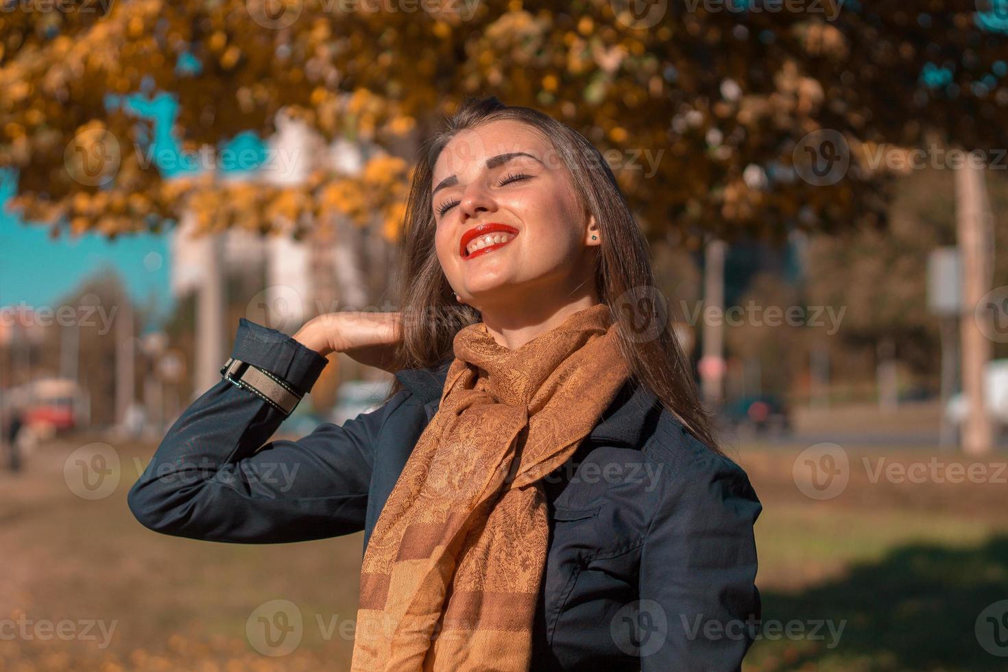 bellissimo ragazza nel un' lungo sciarpa sollevato sua testa e chiuso occhi per il sole foto