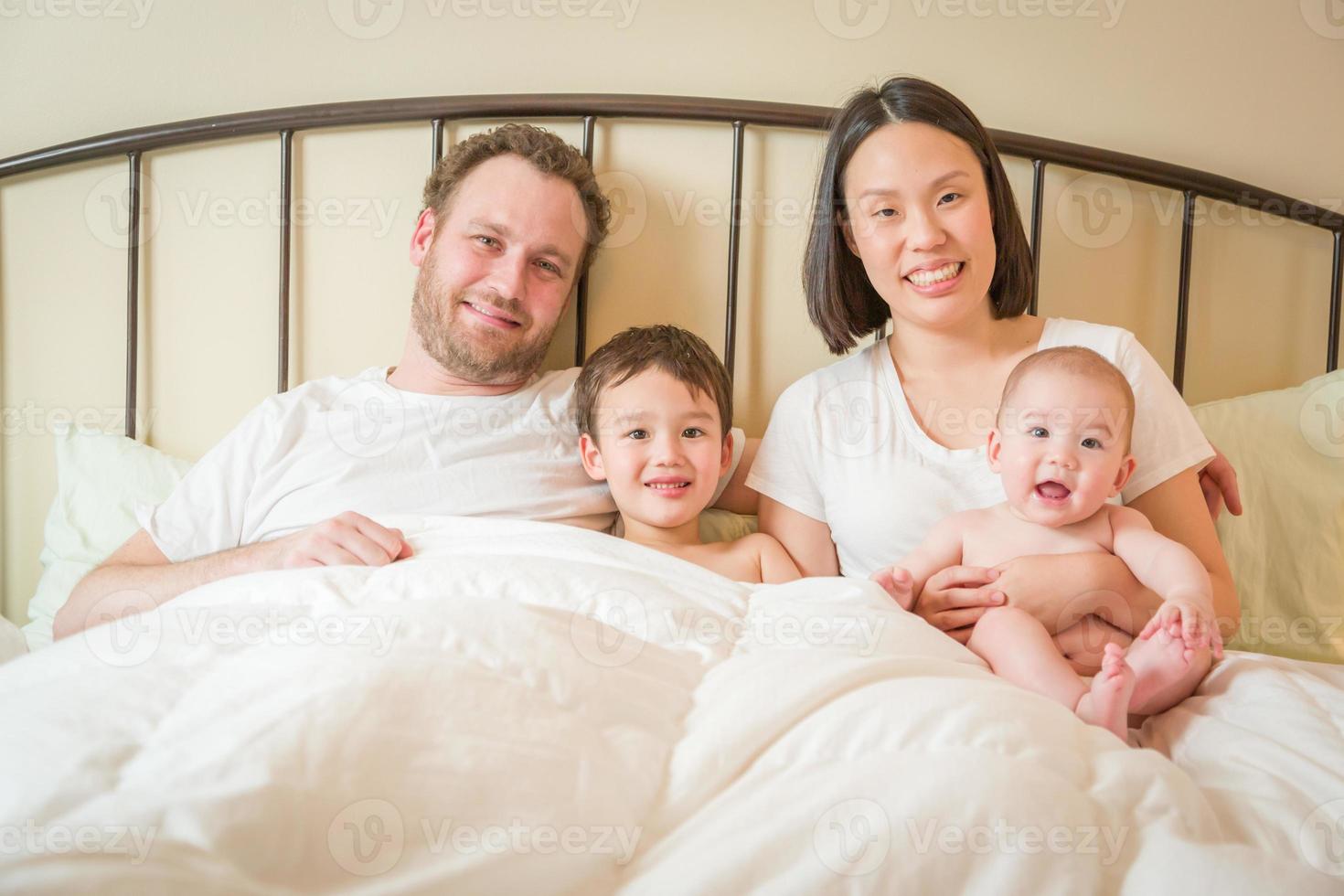 misto gara Cinese e caucasico bambino ragazzi posa nel letto con loro padre e madre foto