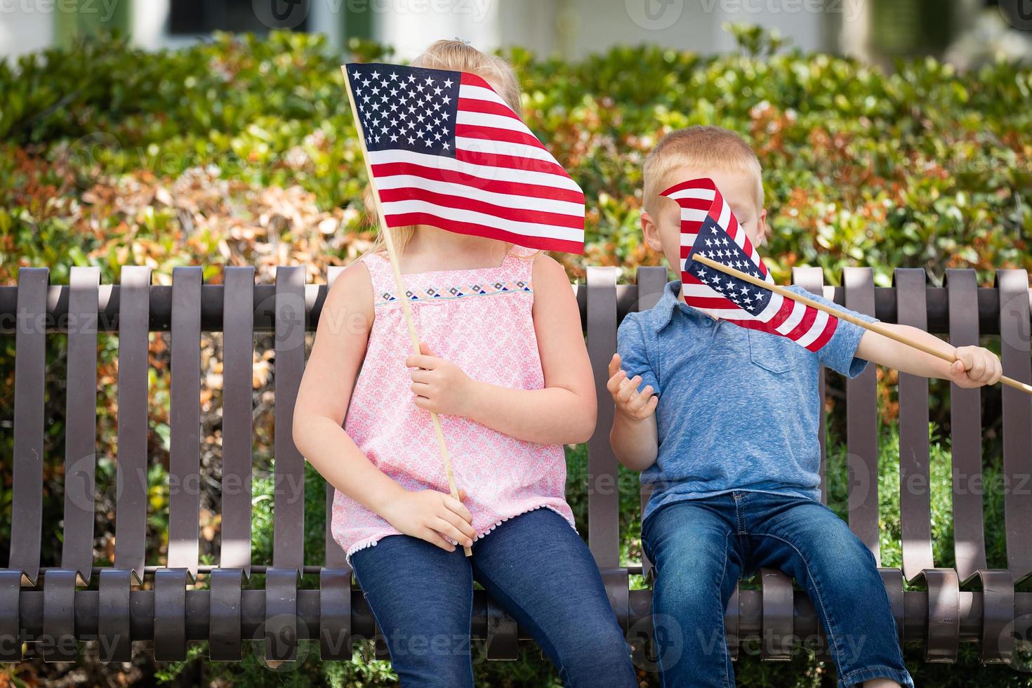 giovane sorella e fratello agitando americano bandiere su il panchina a il parco foto