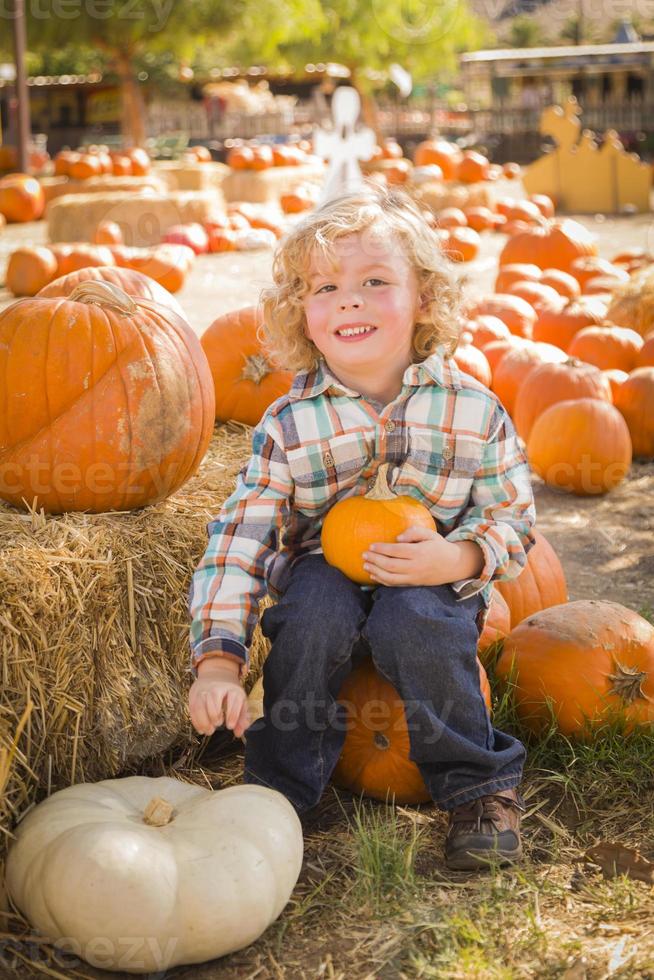 poco ragazzo seduta e Tenere il suo zucca nel un' rustico ranch ambientazione a il zucca toppa. foto