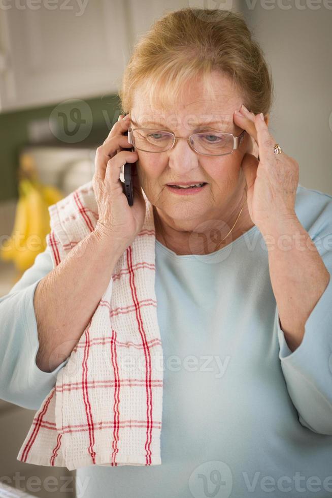 scioccato anziano adulto donna su cellula Telefono nel cucina foto